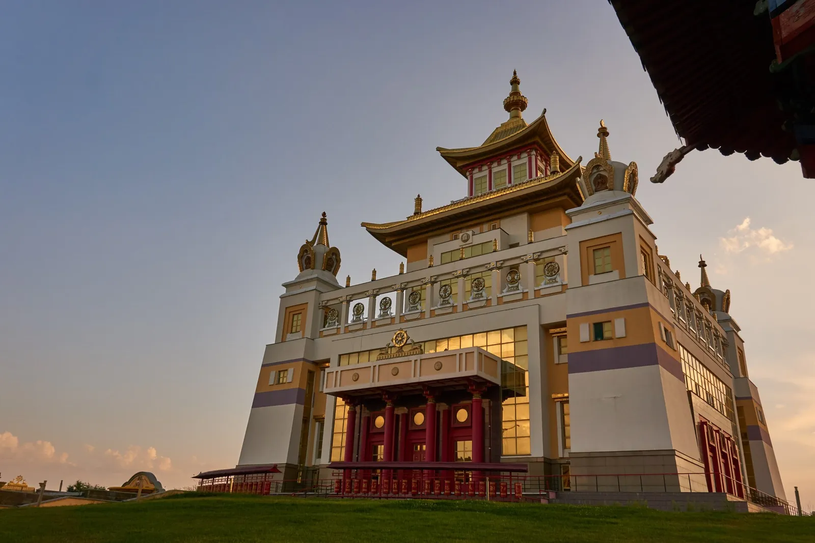 A white Buddhist temple with golden roofs under an open sky, stupas in front.