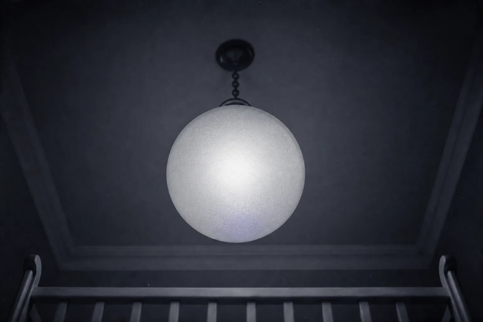 Looking up from a child's cot: a round frosted lamp on a short chain overhead, a high white ceiling at the edges.